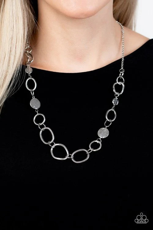 Paparazzi Accessories Industrial Intentions - Silver A mismatched assortment of hammered silver discs, textured silver links, shiny silver rings, and asymmetrical silver links boldly interlock below the collar for a gritty fashion. Features an adjustable
