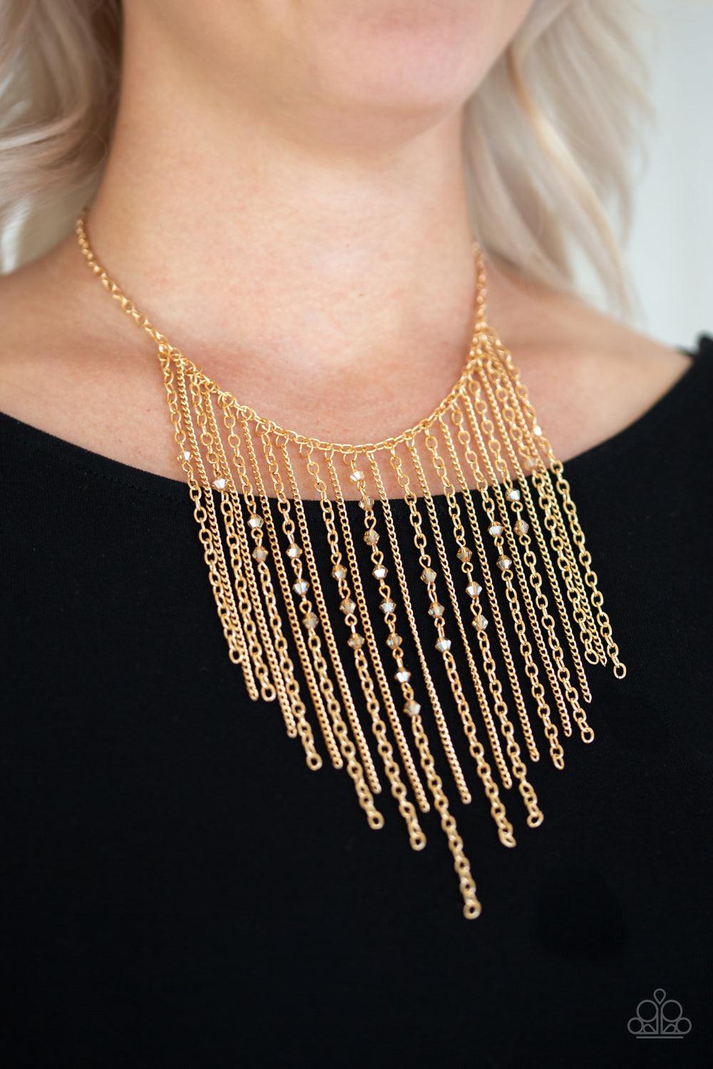 Paparazzi Accessories First Class Fringe - Gold Varying in length, mismatched gold chains stream from the bottom of a classic gold chain. Faceted golden crystal-like beads sporadically dot the free-falling chains, creating a statement-making fringe below