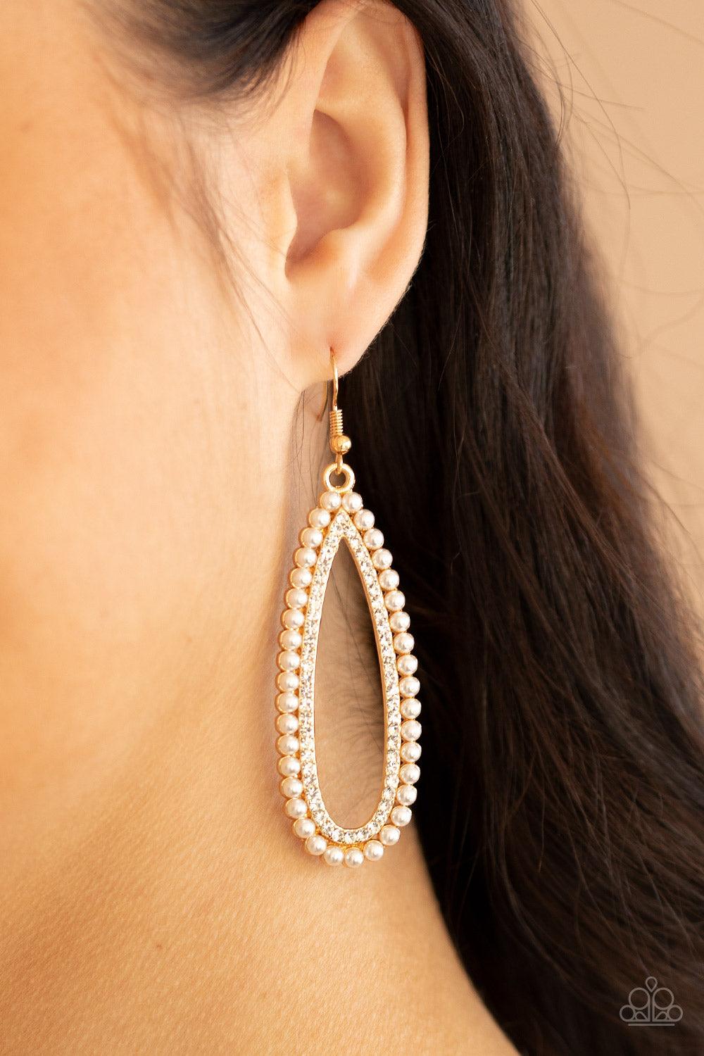 Paparazzi Accessories Glamorously Glowing - Gold A collection of dainty white pearls surrounds a glittery row of glassy white rhinestones, stacking into a vintage inspired teardrop frame. Earring attaches to a standard fishhook fitting. Sold as one pair o