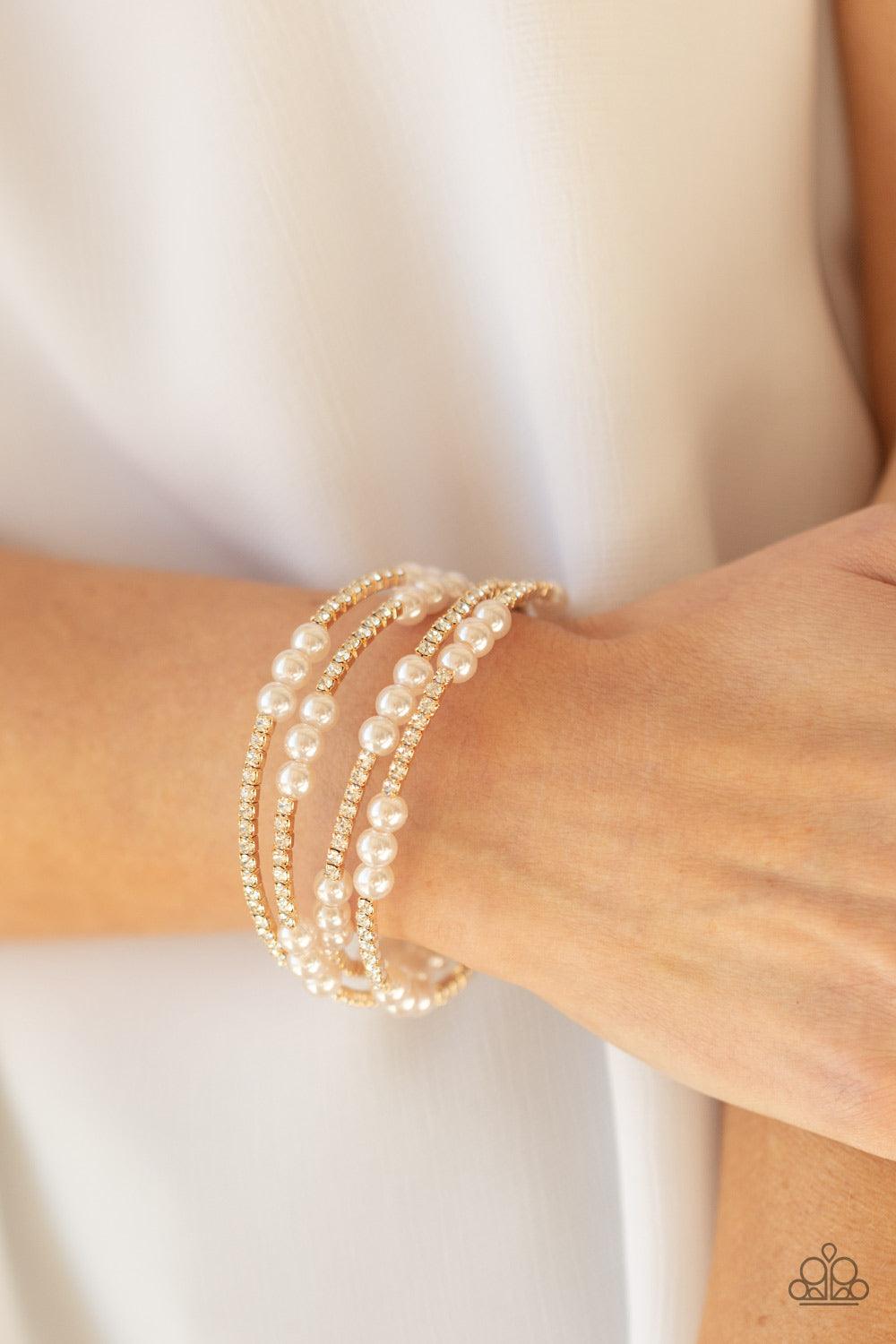 Paparazzi Accessories Hollywood Hospitality - Gold Sparkly sections of glassy white rhinestones and classic pearls are delicately threaded along a coiled wire, creating a glamorously golden infinity wrap style around the wrist. Sold as one individual brac