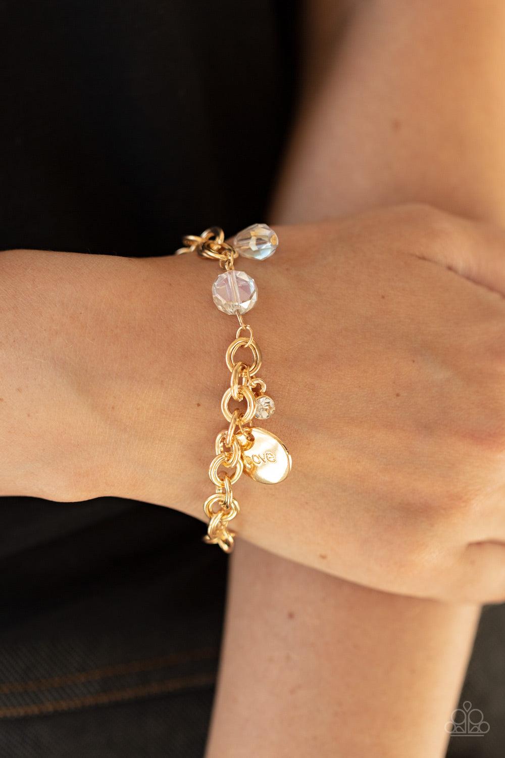 Paparazzi Accessories Lovable Luster - Gold White crystal-like beads, a dainty white rhinestone, and a gold disc stamped in the word, "love," adorn a double-linked gold chain, creating a flirty fringe around the wrist. Features an adjustable clasp closure
