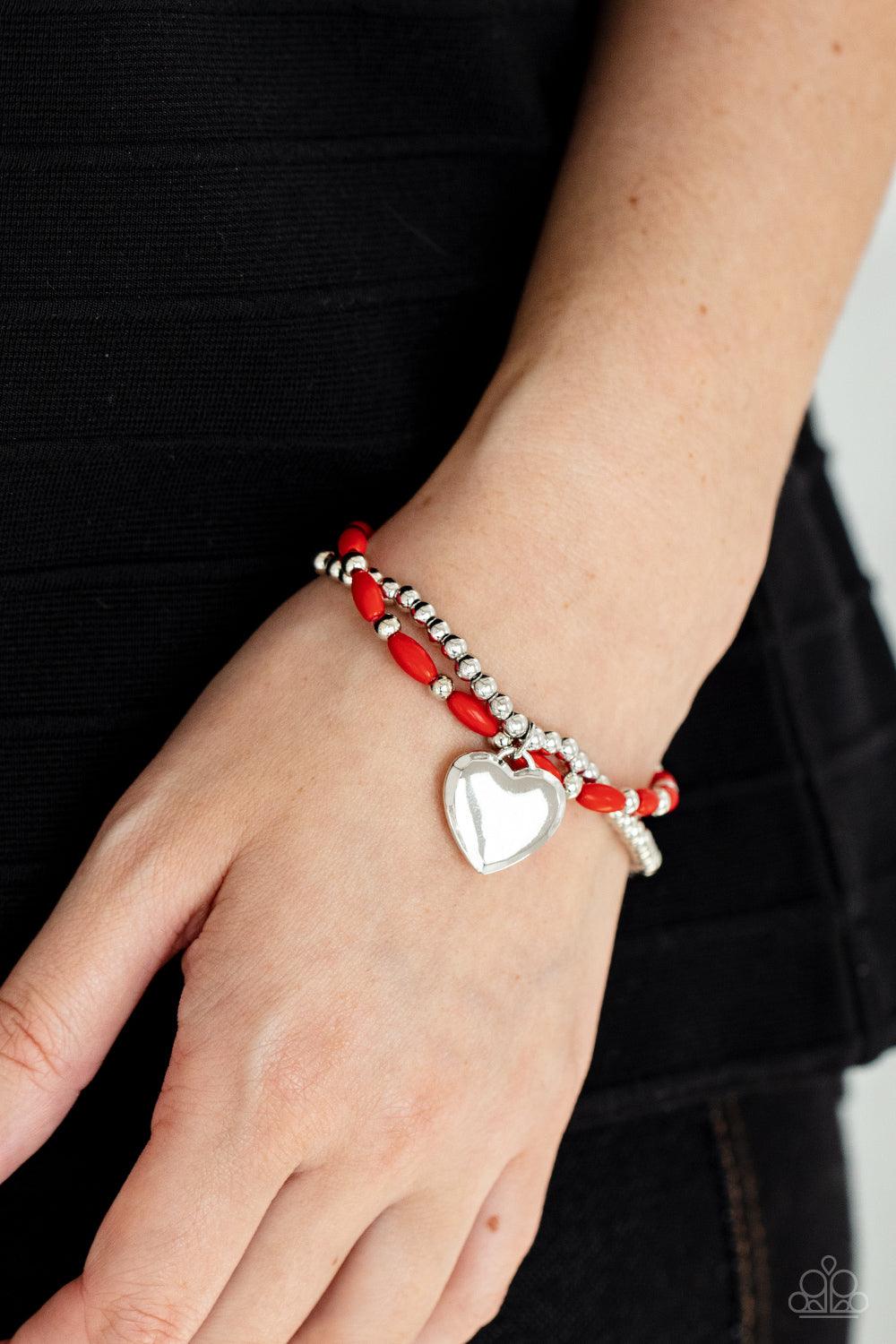 Paparazzi Accessories Candy Gram - Red A shiny silver heart dangles from a strand of fiery red beads. It is paired with a strand of round silver beads threaded along a stretchy band for a whimsical display around the wrist. Sold as one pair of bracelets.