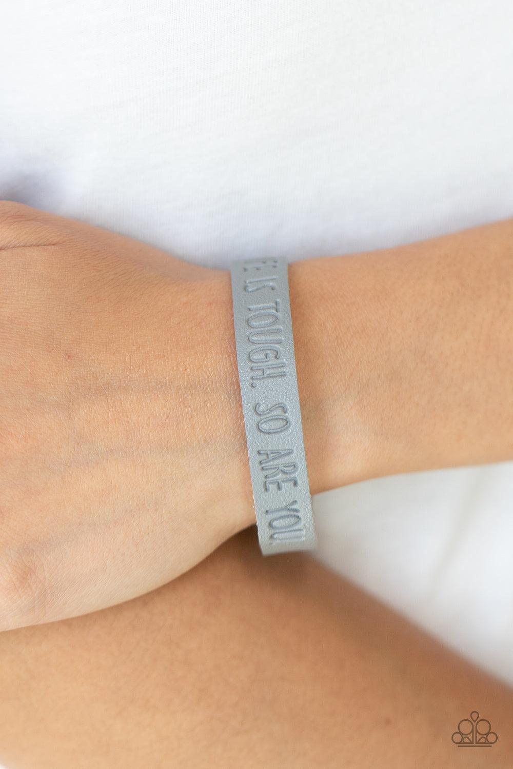 Paparazzi Accessories Life is Tough - Silver A dainty gray leather band is stamped in the phrase, "Life is tough. So Are You.," creating an inspiring centerpiece around the wrist. Features an adjustable snap closure. Sold as one individual bracelet. Jewel
