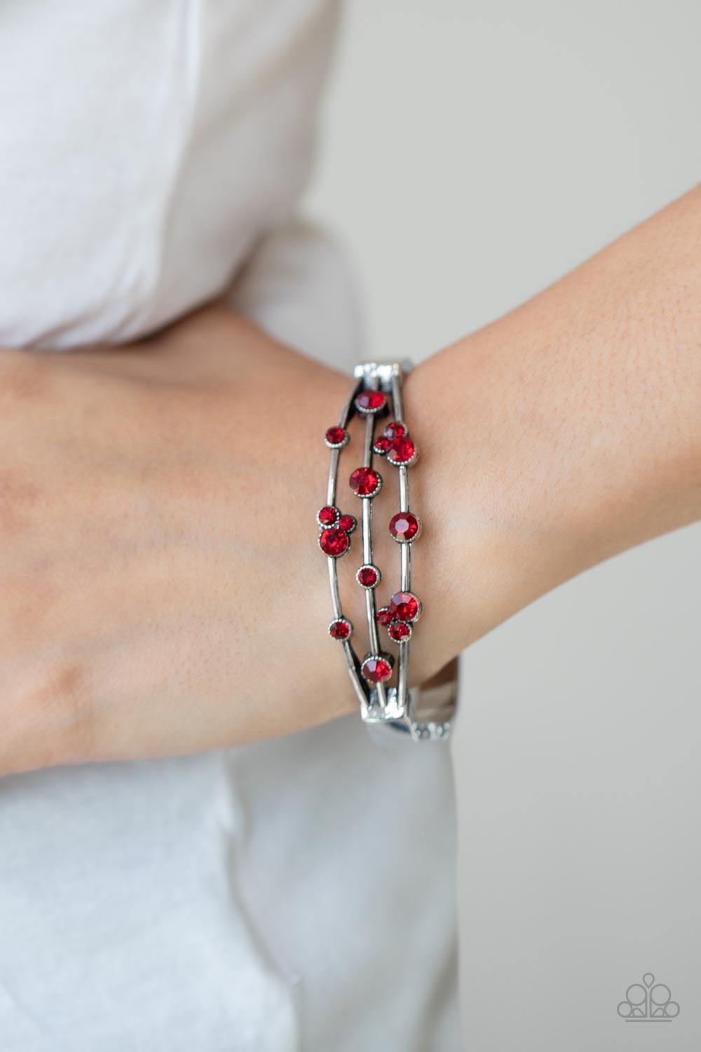 Paparazzi Accessories Cosmic Candescence - Red A smattering of fiery red rhinestones adorn three silver bars that coalesce into a versatile silver cuff-like bangle around the wrist. Features a hinged closure. Sold as one individual bracelet. Jewelry