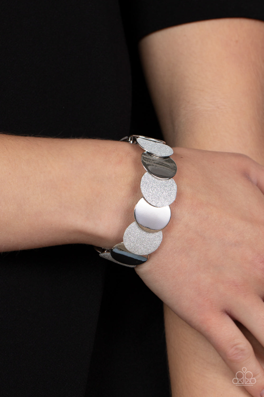 Paparazzi Accessories Demurely Disco - Silver A glimmering collection of shiny silver discs and glitter coated silver discs delicately overlap along stretchy bands around the wrist, creating a dazzling hint of shimmer. Sold as one individual bracelet. Bra