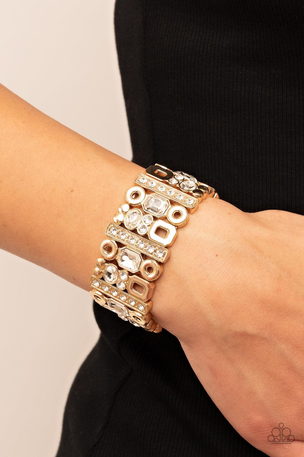 Paparazzi Accessories Dynamically Diverse - Gold Infused with flat gold studs and geometric gold accents, a mismatched assortment of oval, round, and emerald style white rhinestones coalesce into edgy frames along a stretchy band for an intense sparkle ar