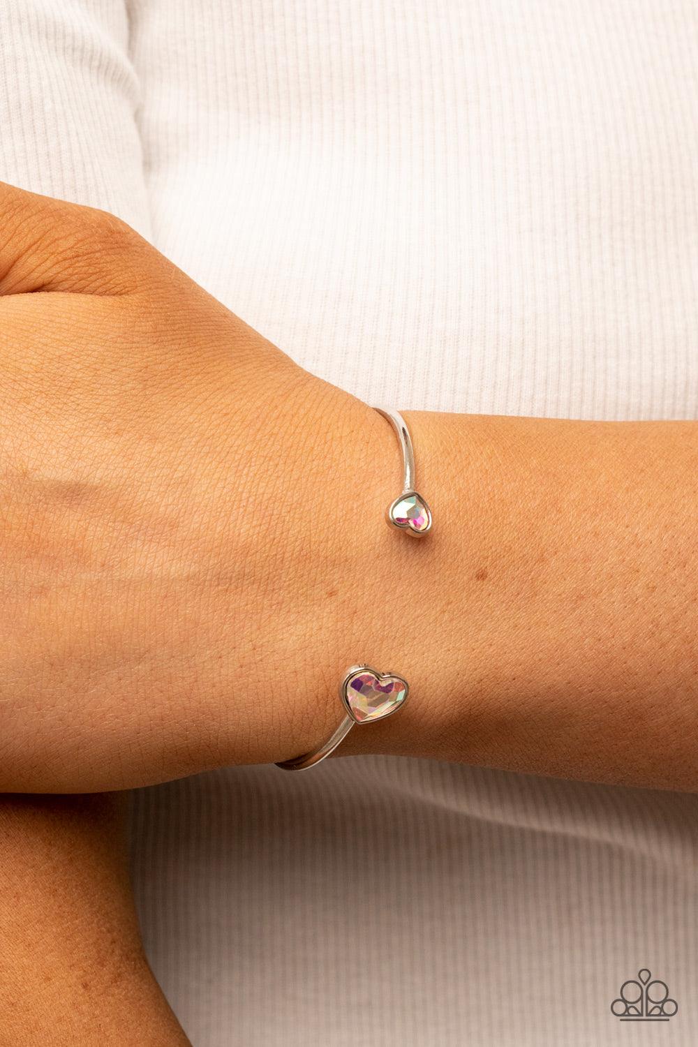 Paparazzi Accessories Unrequited Love - Multi Enhanced with iridescent rhinestones, two silver hearts adorn the ends of a silver band that curls around the wrist for a flirtatious open-faced style cuff. Sold as one individual bracelet. Bracelets