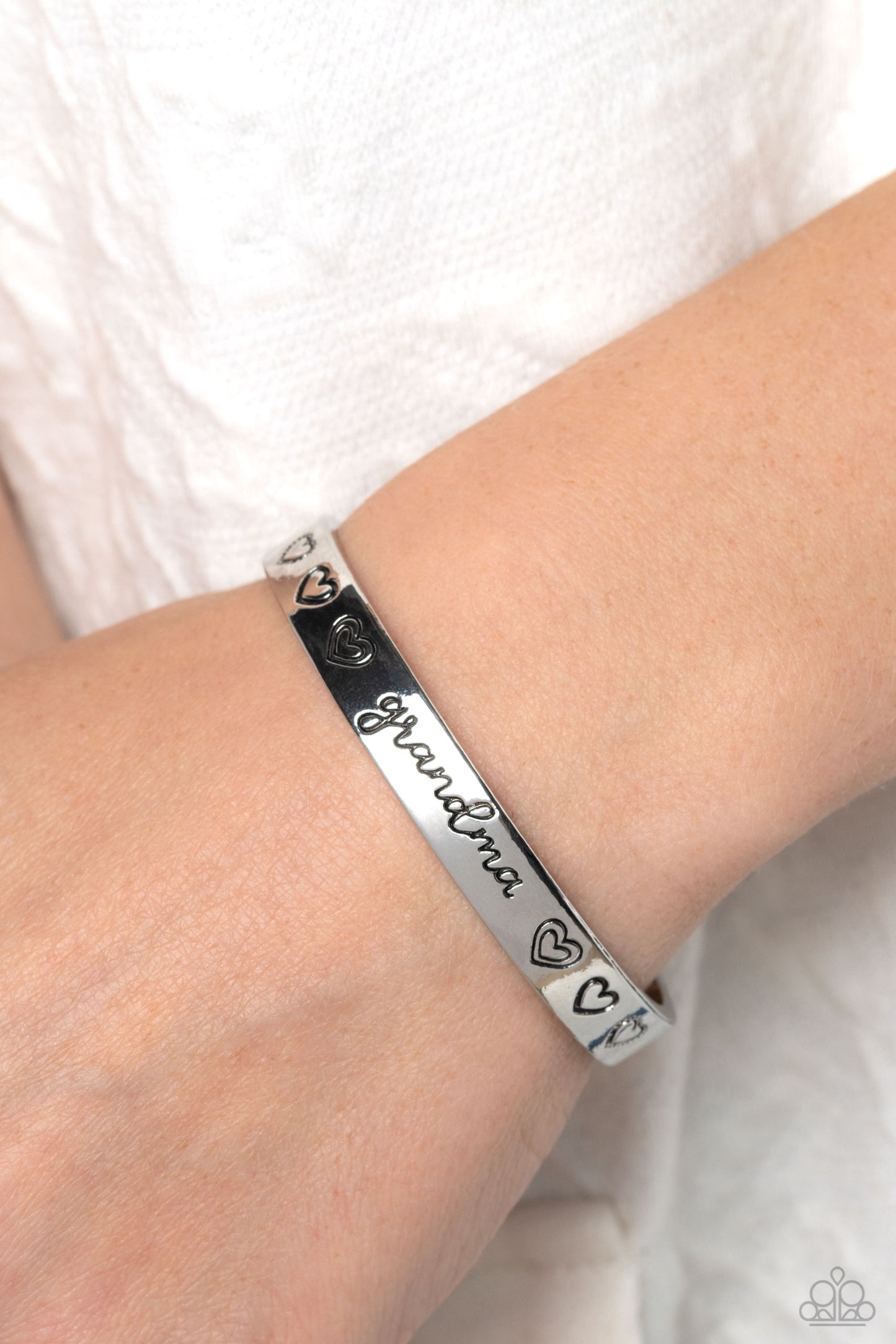Paparazzi Accessories A Grandmothers Love - Silver Brushed in a polished sheen, a skinny silver bar curls around the wrist, creating a rustic cuff. Featuring a heart motif, the skinny cuff is engraved with the word “grandma” with various styles of hearts