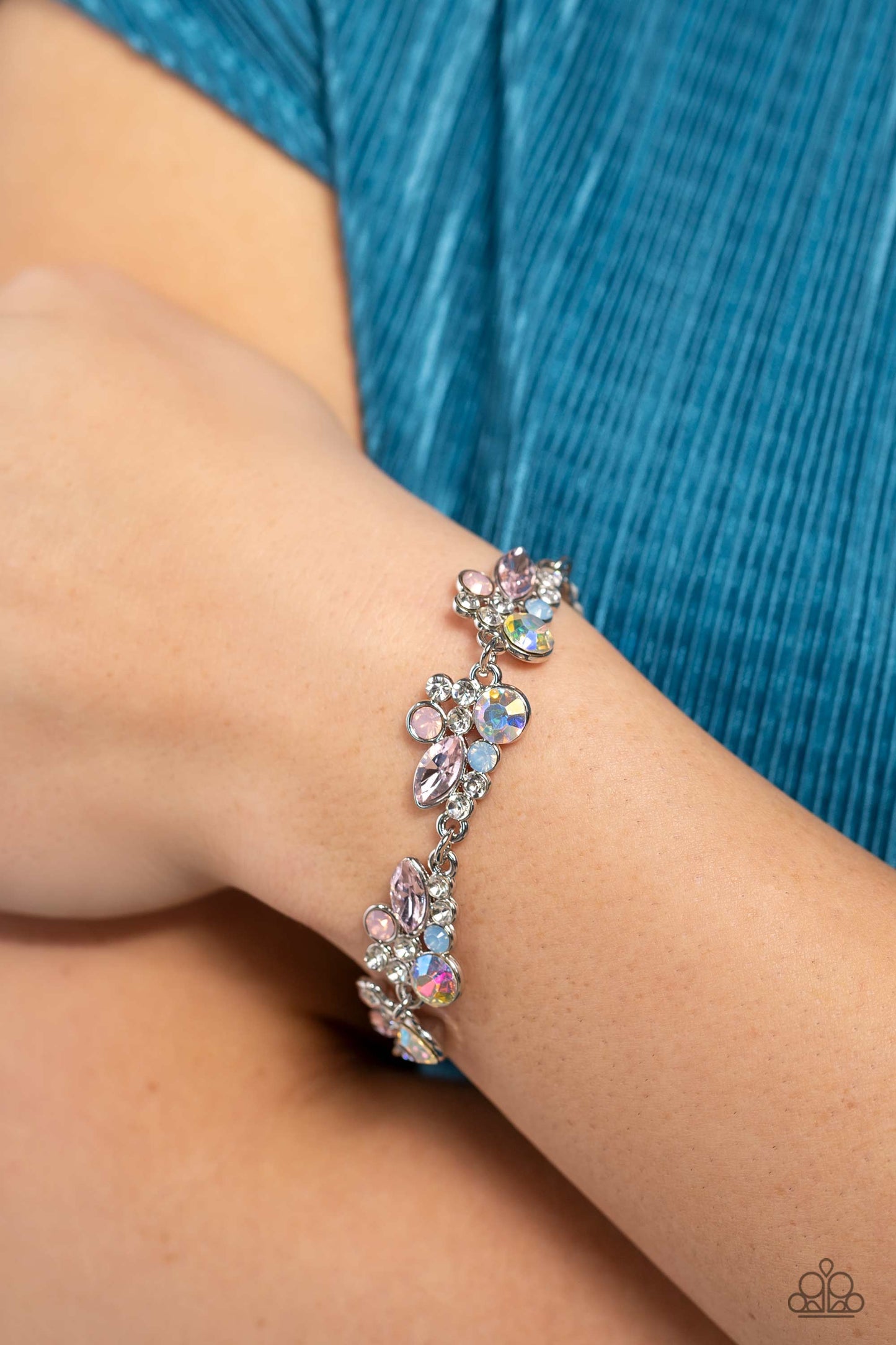 Paparazzi Accessories Poolside Perfection - Multi An eclectic collection of white, blue, iridescent and light peach round rhinestones in varying sizes and marquise-cut gems in a light pink shade cluster around the wrist in high-sheen silver frames. Patter