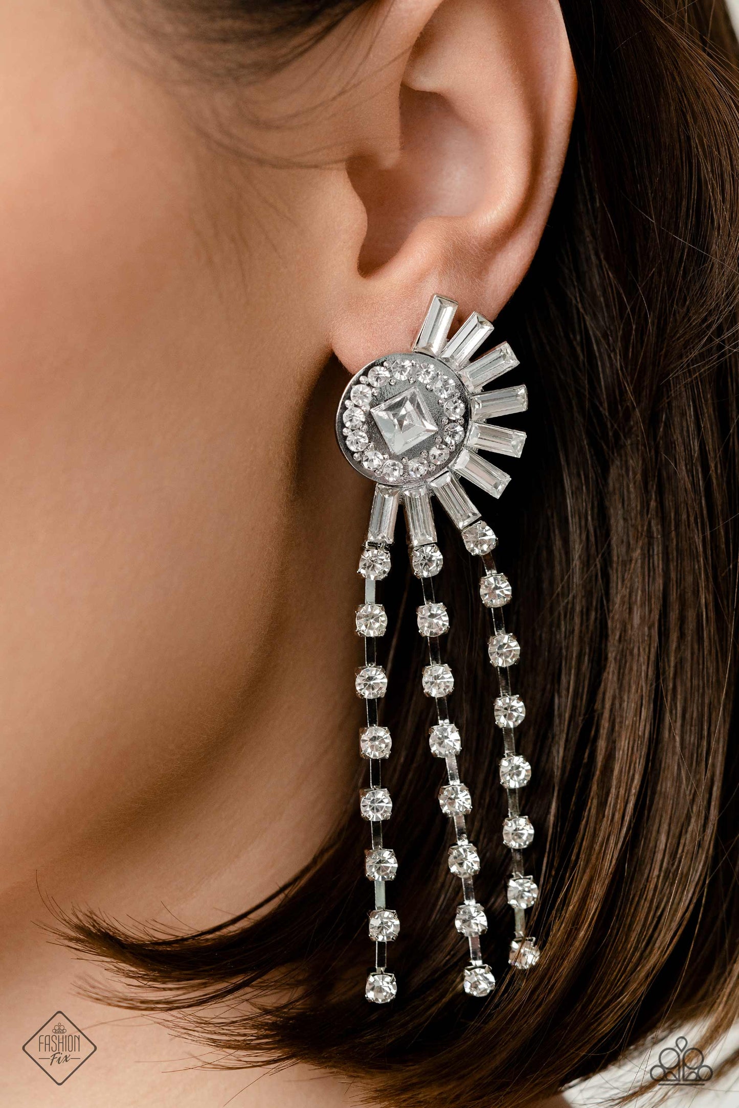 Paparazzi Accessories Torrential Twinkle - White Encased in square silver fittings, three strands of dainty, glistening, white gems cascade from a blindingly ornate circular frame. Emerald-cut white gems explode from the rhinestone-dusted frame for additi