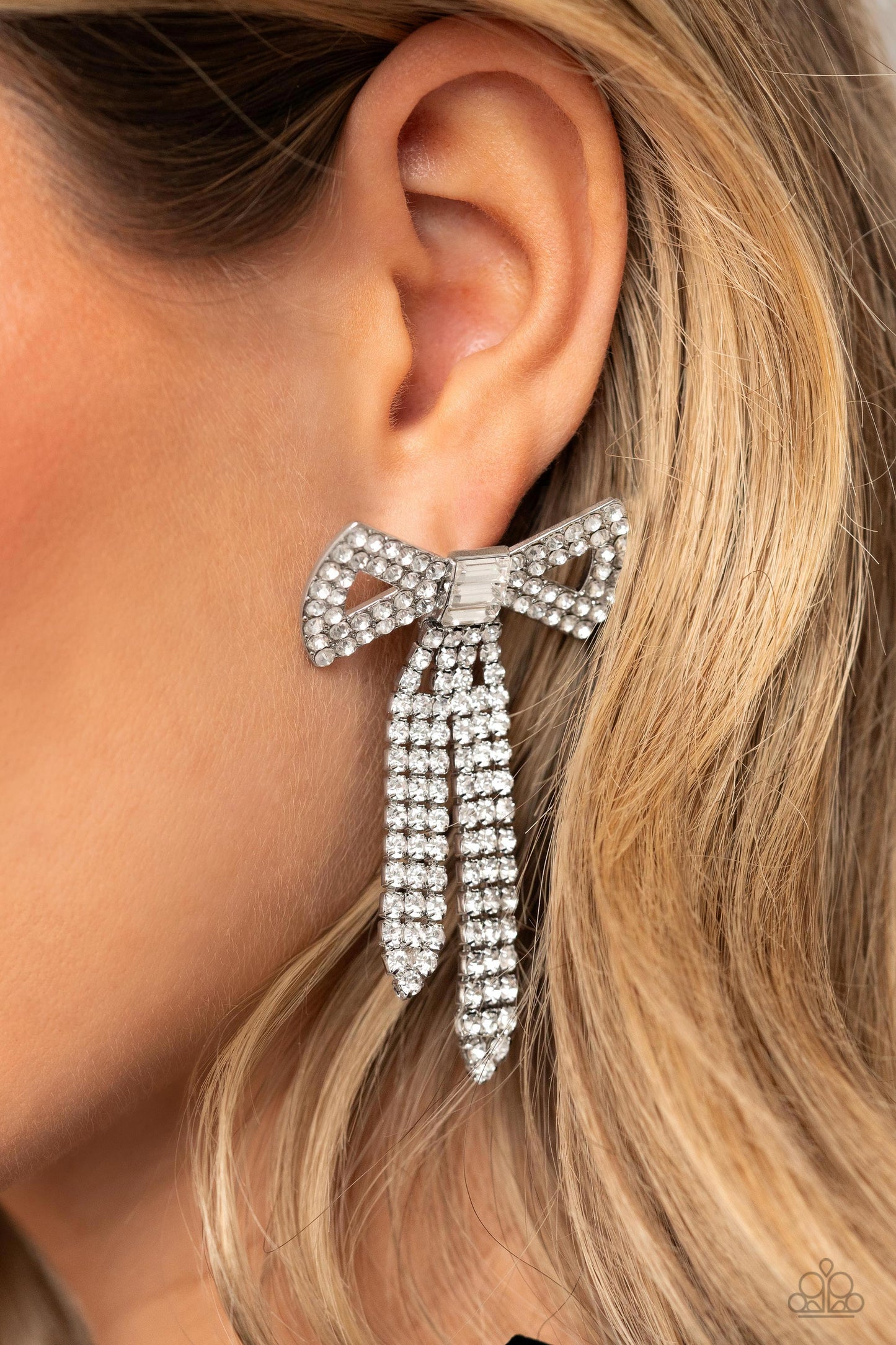 Paparazzi Accessories Just BOW With It - White Featuring silver square fittings, high-sheen bands of silver, adorned in sparkling white rhinestones loop into a stunning bow charm, creating a classy statement at the ear. Featured in the center of the class