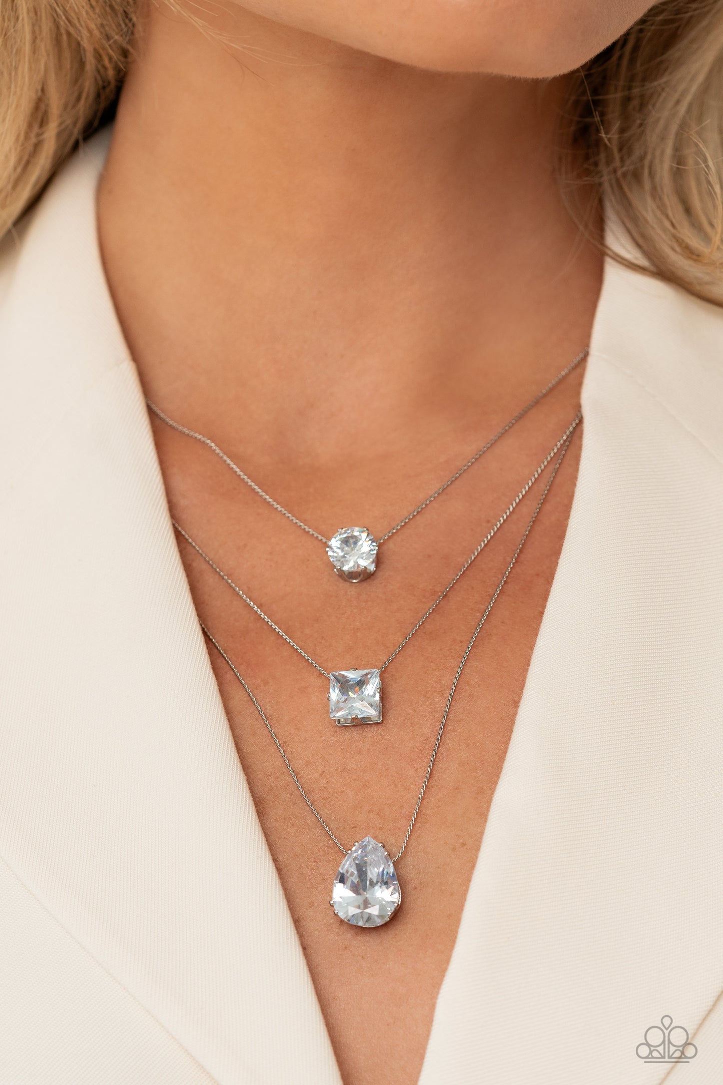 Paparazzi Accessories Lustrous Layers - White Featuring a subtle iridescent finish, exaggerated, faceted round, square, and teardrop gems layer down the chest from three sleek silver dainty chains, in a refined fashion. Features an adjustable clasp closur