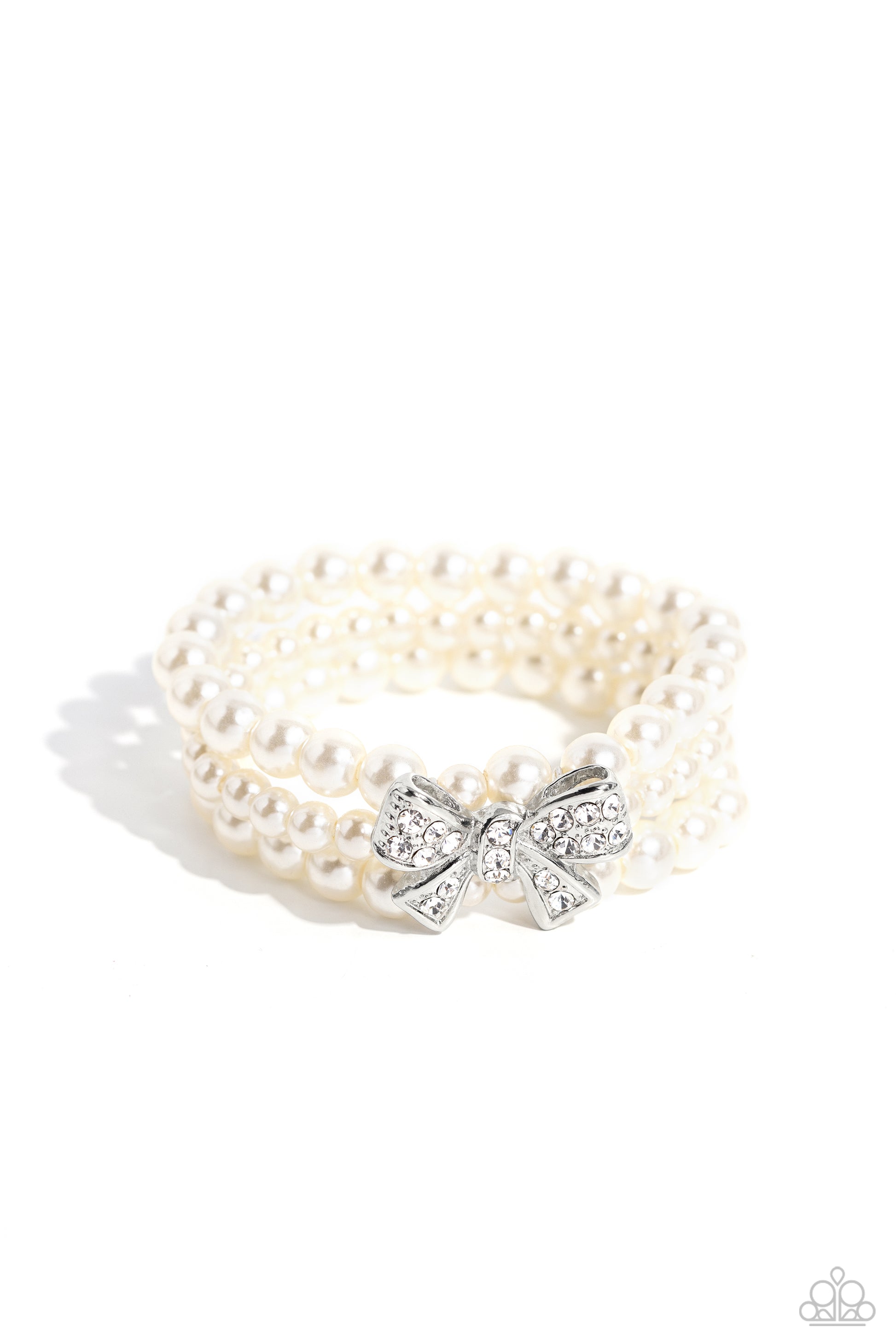 Paparazzi Accessories How Do You Do? - White Strung along elastic stretchy bands, three strands of high-sheen classic white pearls wrap around the wrist. Featured atop the pearly collection, a loopy silver bow, filled with glistening white rhinestones is