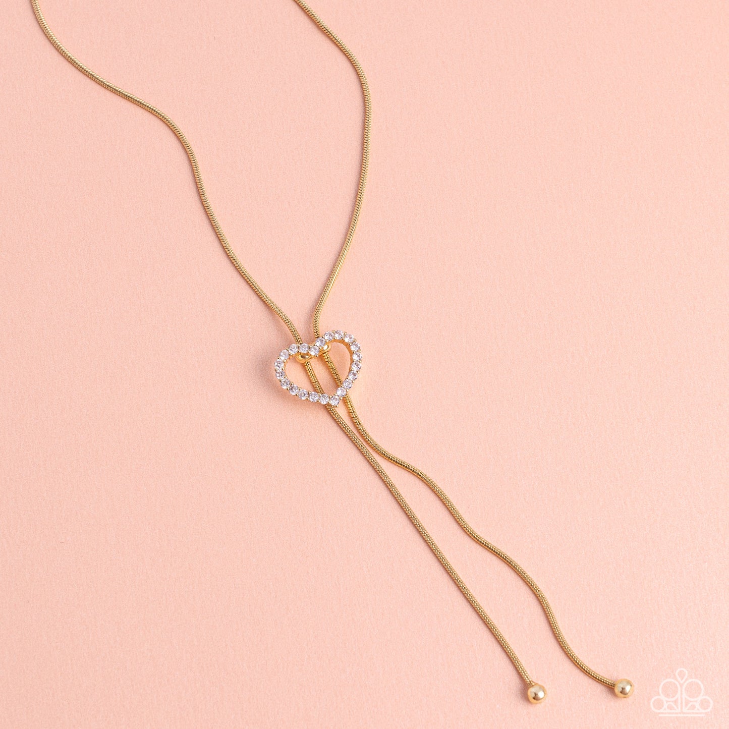 Paparazzi Accessories Tempting Tassel - Gold A dainty white rhinestone-encrusted heart silhouette slides along dainty strands of glistening gold snake chain for a timeless, refined tassel. Features a bolo closure. Sold as one individual necklace. Includes