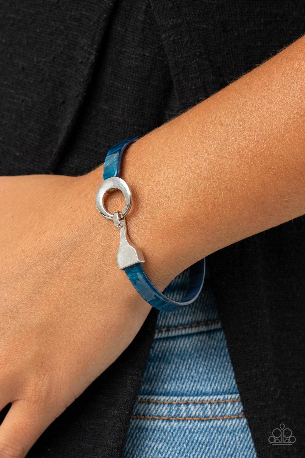 Paparazzi Accessories HAUTE Button Topic - Blue Featuring a shell-like shimmer, a dainty blue acrylic band curls around the wrist, connecting to a silver hinged fitting at the center. Features a hinged closure. Sold as one individual bracelet. Jewelry