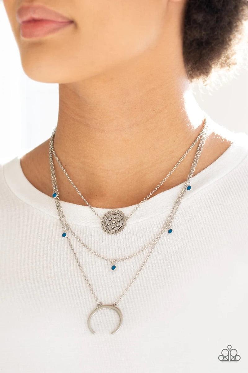 Paparazzi Accessories Lunar Lotus - Blue A silver floral frame swings from the uppermost chain, above a strand of faceted blue beads swinging from a shimmery silver chain. A silver crescent frame swings from the lowermost chain, creating whimsical layers