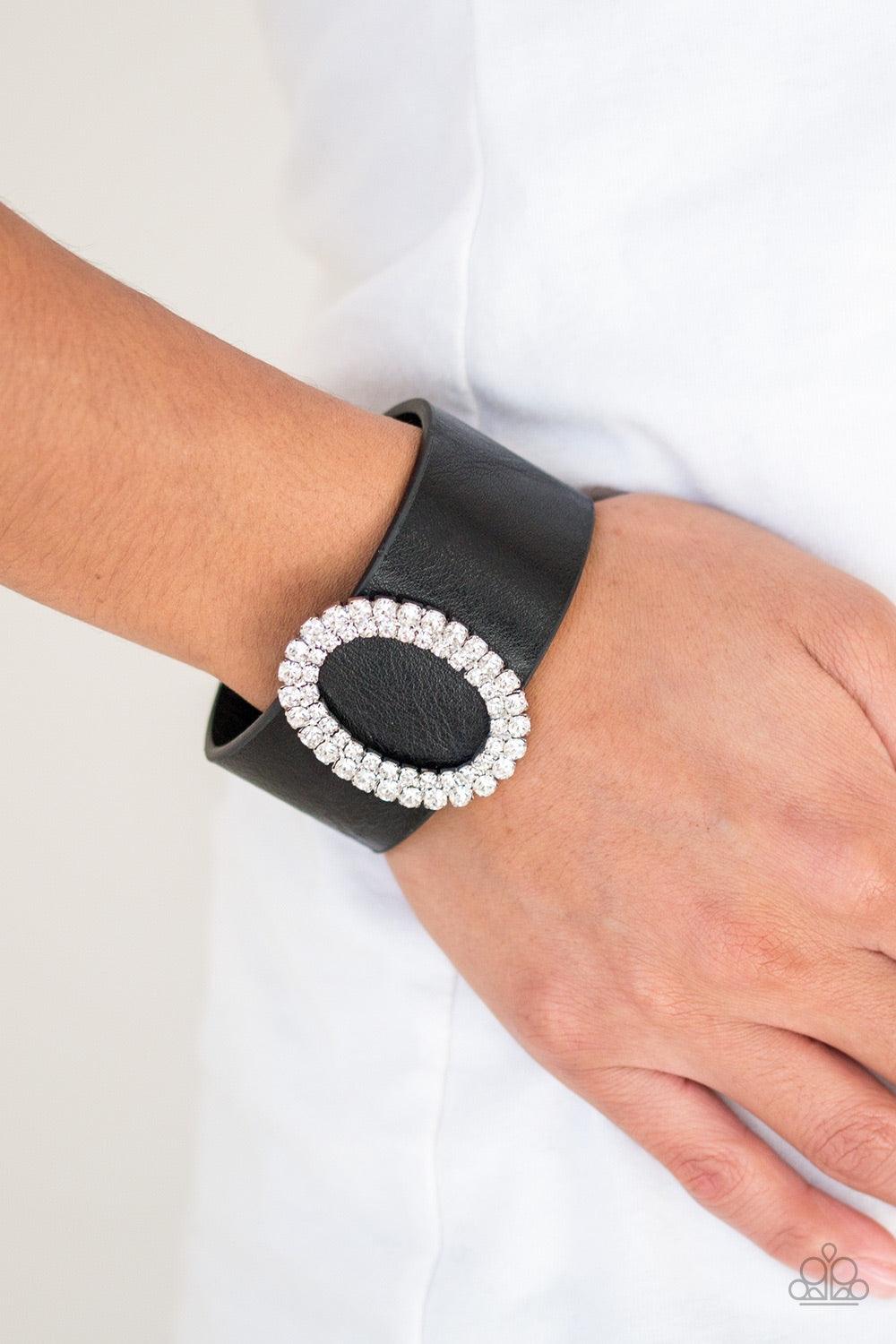 Paparazzi Accessories Center Stage Starlet - Black Encrusted in glassy white rhinestones, a round silver frame slides along a thick black leather band for a glamorous look. Features an adjustable snap closure. Jewelry
