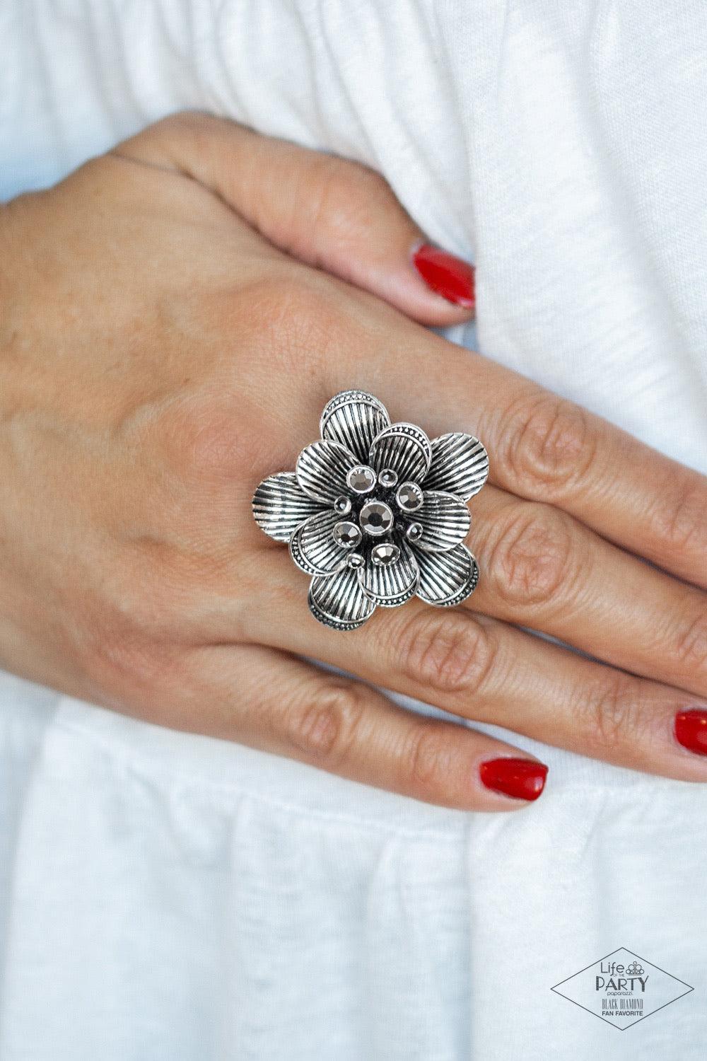 Paparazzi Accessories Petal Pusher - Silver Engraved in linear patterns, antiqued silver petals bloom into an oversized floral frame atop the finger. A bouquet of glittery hematite rhinestones burst from the center, creating a sparkling statement piece at