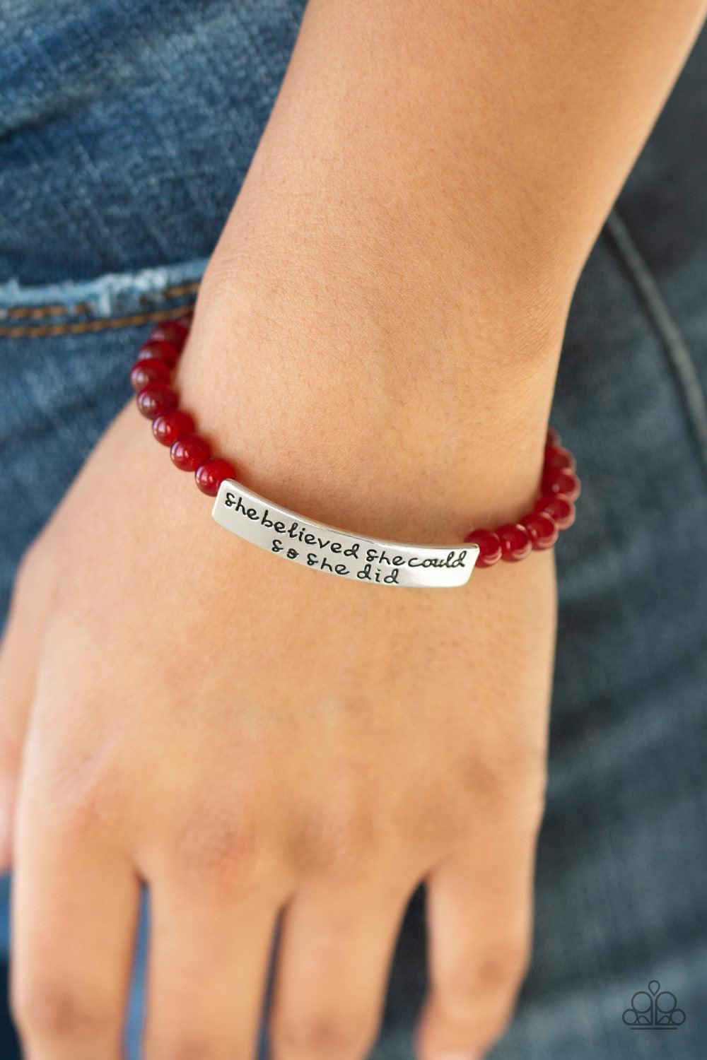 Paparazzi Accessories So She Did - Red A collection of dainty red cat’s eye stone beads and an antiqued frame stamped in the inspirational phrase, “She believed she could, so she did”, are threaded along a stretchy band around the wrist for a whimsical fa
