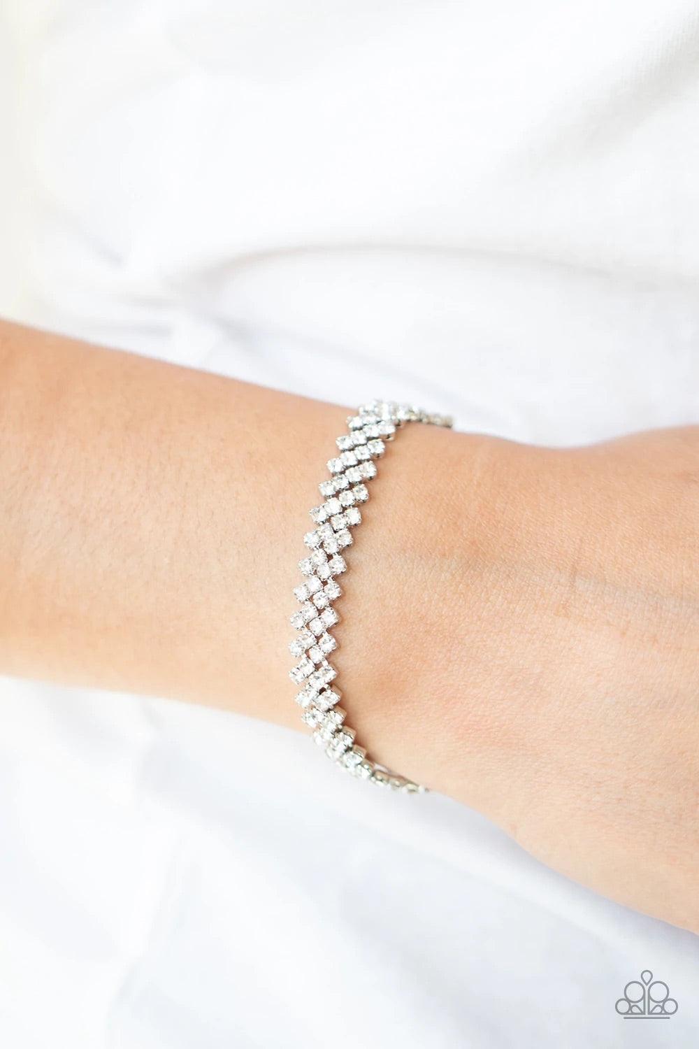 Paparazzi Accessories Chicly Candescent - White Featuring sleek silver fittings, dainty rows of glassy white rhinestones delicately slant across the wrist, coalescing into a timeless centerpiece. Features an adjustable clasp closure. Sold as one individua