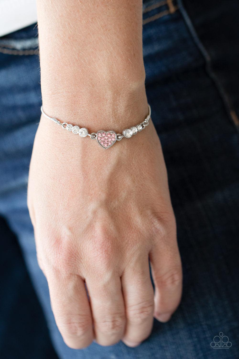 Paparazzi Accessories Big-Hearted Beam - Pink A trio of glassy white rhinestones flank a shiny silver heart charm, creating a flirty centerpiece. Glittery pink rhinestones dot the dainty heart, adding a splash of color to the glittery display. Features an