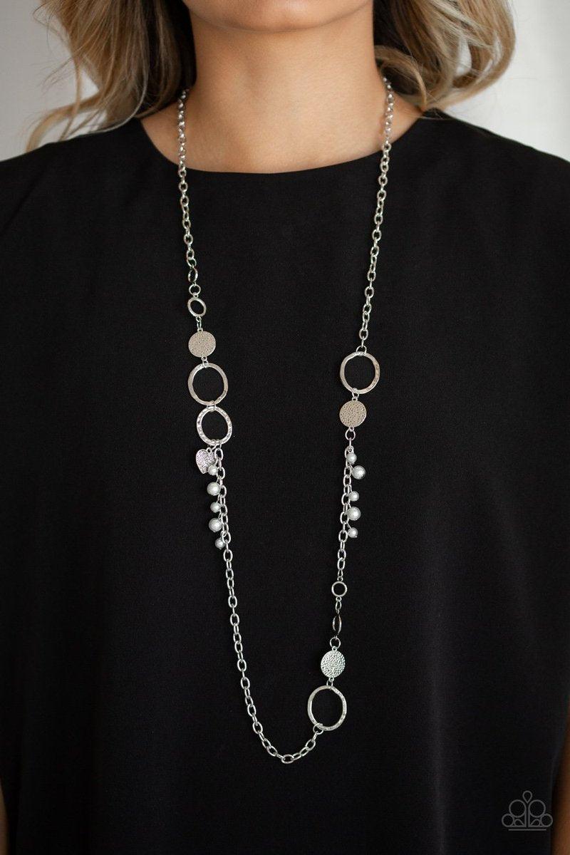 Paparazzi Accessories Unapologetic Flirt - Silver Infused with sections of shimmery silver chains, an assortment of hammered silver discs and silver rings link across the chest. A collection of pearly beads and dainty silver heart charms asymmetrically do