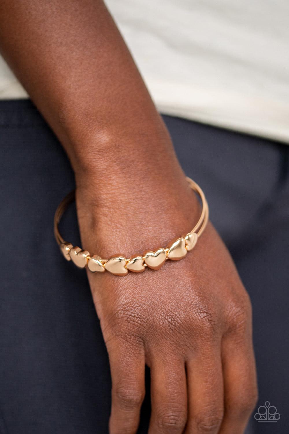 Paparazzi Accessories Totally Tenderhearted - Gold A charming collection of gold heart frames coalesce around a doubled gold bangle, creating a whimsical centerpiece. Jewelry