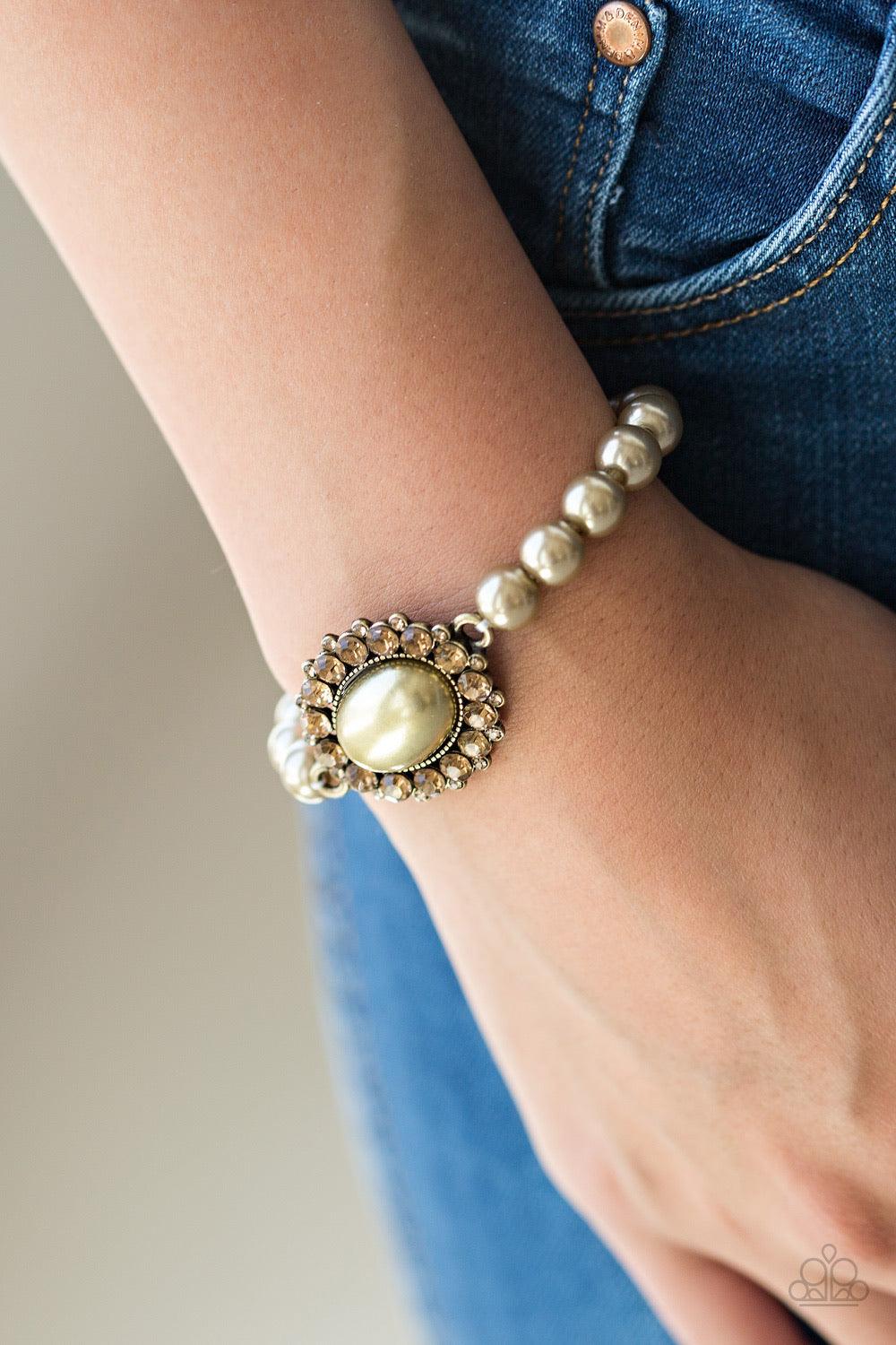 Paparazzi Accessories Starry-Eyed Starlet - Brass Pearly brass beads are threaded along an elastic stretchy band. A large brass pearl is pressed into the center of a topaz rhinestone encrusted frame, creating a dramatic centerpiece atop the wrist. Sold as