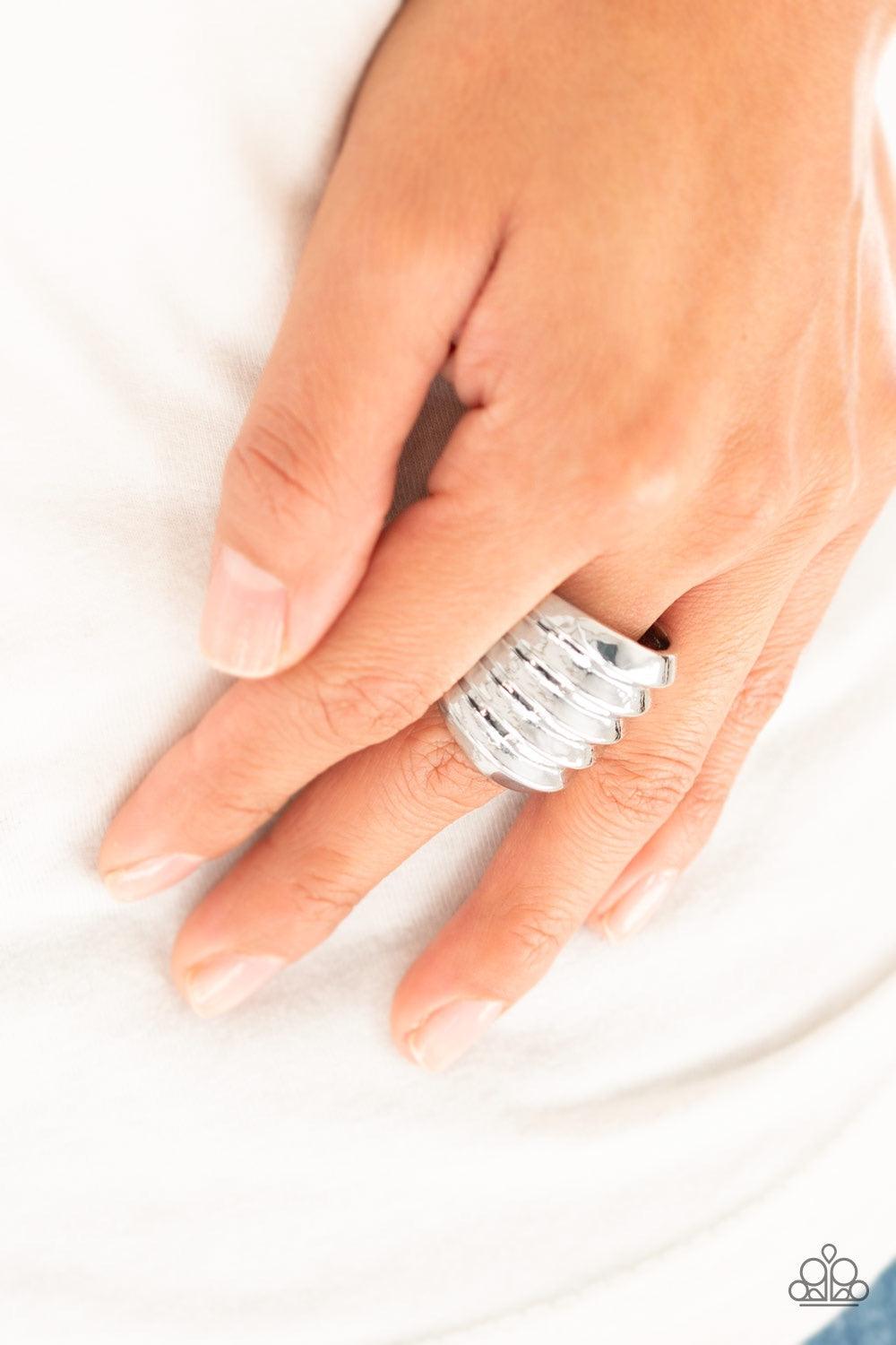 Paparazzi Accessories Hit Em Where It Hurts - Silver Rippling silver bands coalesce into a thick frame around the finger for a dramatic industrial look. Features a stretchy band for a flexible fit. Jewelry