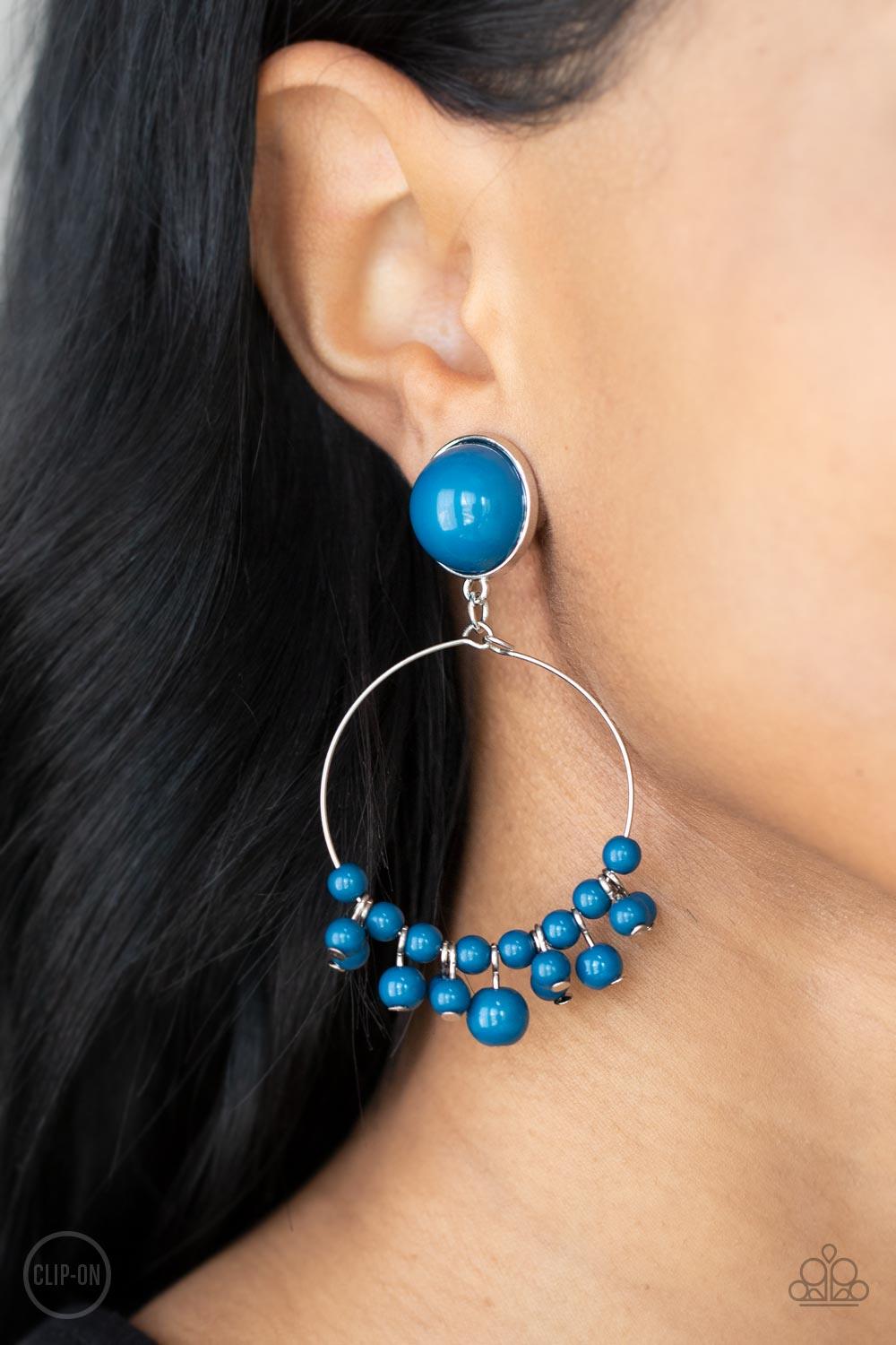 Paparazzi Accessories Cabaret Charm - Blue Shiny blue beads are threaded along a dainty wire hoop that attaches to an oversized blue beaded fitting, creating a bubbly fringe. Earring attaches to a standard clip-on fitting. Sold as one pair of clip-on earr