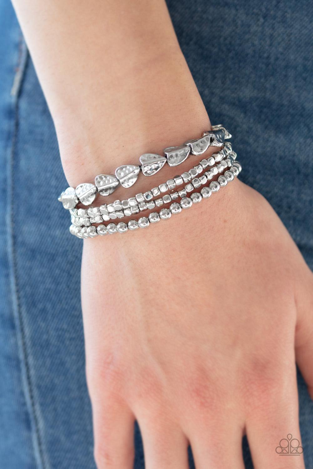 Paparazzi Accessories Ancient Heirloom - Silver A collection of silver cubes, classic silver beads, and hammered spade-like beading is threaded along stretchy bands around the wrist for a boldly stacked look. Jewelry