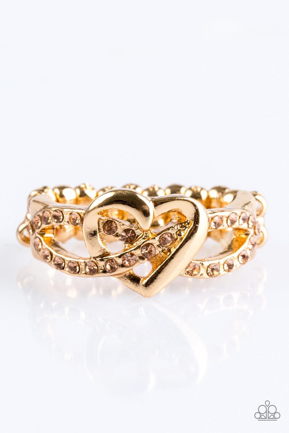 Paparazzi Accessories Heavenly Heart - Gold Encrusted in glittery peach rhinestones, golden ribbons crisscross across the finger, creating a dainty band. A glistening gold heart adorns the center of the band for a romantic finish. Features a dainty stretc