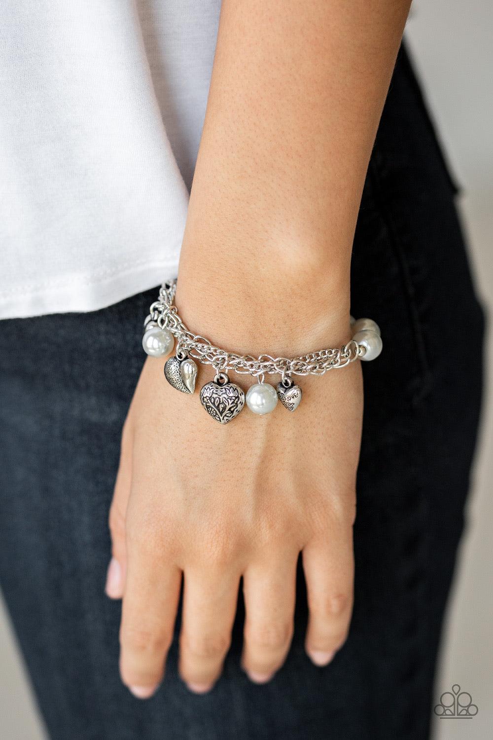 Paparazzi Accessories More Amour - Silver Attached to a section of shimmery silver chain, pearly gray and dainty silver beads are threaded along a stretchy band. Mismatched silver heart charms swing from the glistening chain, creating a flirty fringe. Sol