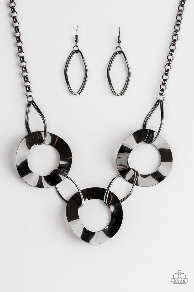 Paparazzi Accessories Modern Mechanics - Black Featuring slightly warped surfaces, asymmetrical gunmetal hoops link with reflective gunmetal rings below the collar for a modern look. Features an adjustable clasp closure. Sold as one individual necklace. I