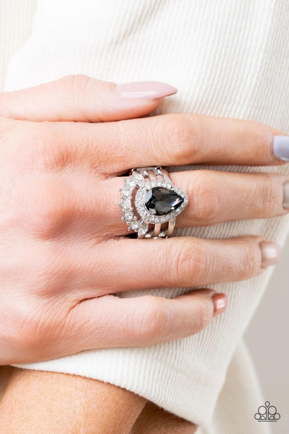 Paparazzi Accessories Elegantly Cosmopolitan - Silver An elegantly oversized smoky teardrop gem, encompassed in a dainty rhinestone frame, sits atop three airy silver bars. A row of classic white rhinestones curves beneath the gem for a glamorous finish.