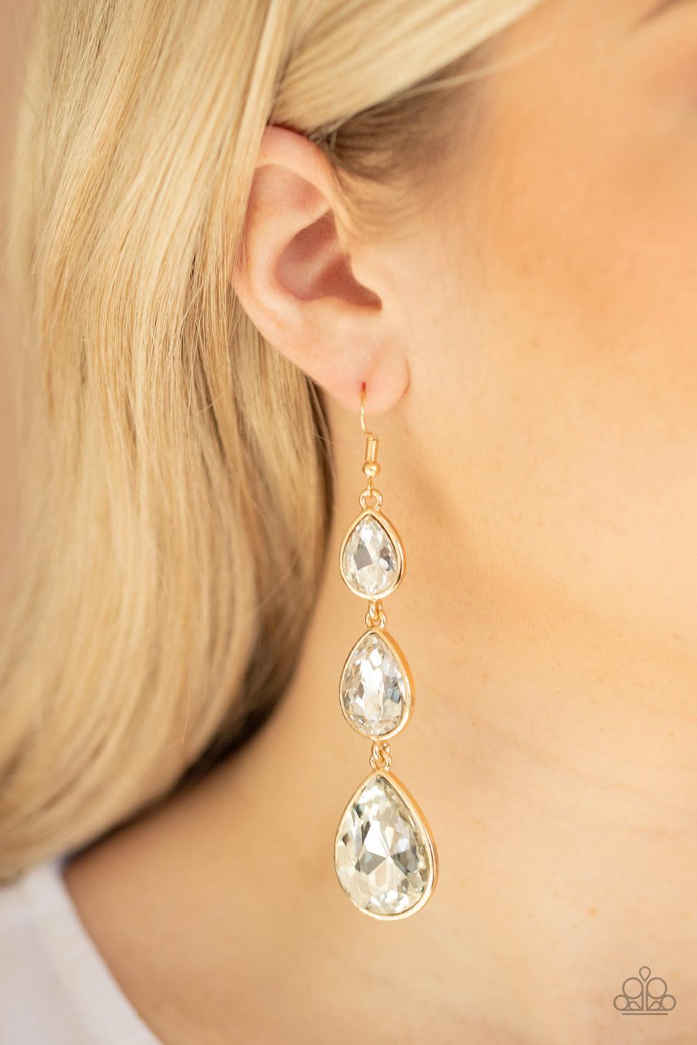 Paparazzi Accessories Metro Momentum - Gold Featuring sleek gold frames, exaggerated white teardrop rhinestones gradually increase in size as they drip from the ear. Earring attaches to a standard fishhook fitting. Sold as one pair of earrings. Jewelry