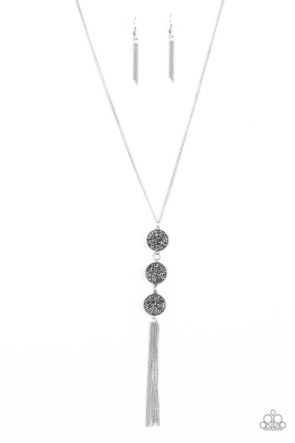 Paparazzi Accessories Triple Shimmer - Silver Sprinkled in smoky and hematite prism style rhinestones, three sparkling silver frames trickle down the chest. A shimmery silver tassel swings from the bottom of the triple stacked pendant for a glamorous fini