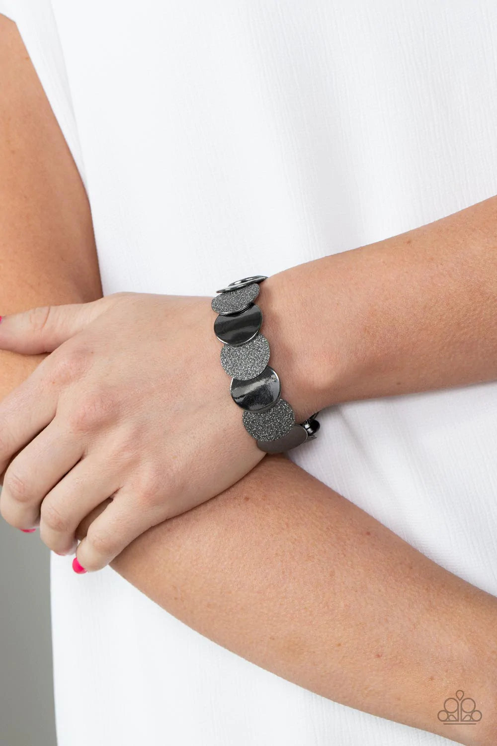 Paparazzi Accessories Demurely Disco - Black A glimmering collection of glistening gunmetal discs and glitter coated gunmetal discs delicately overlap along stretchy bands around the wrist, creating a dazzling hint of shimmer. Sold as one individual brace