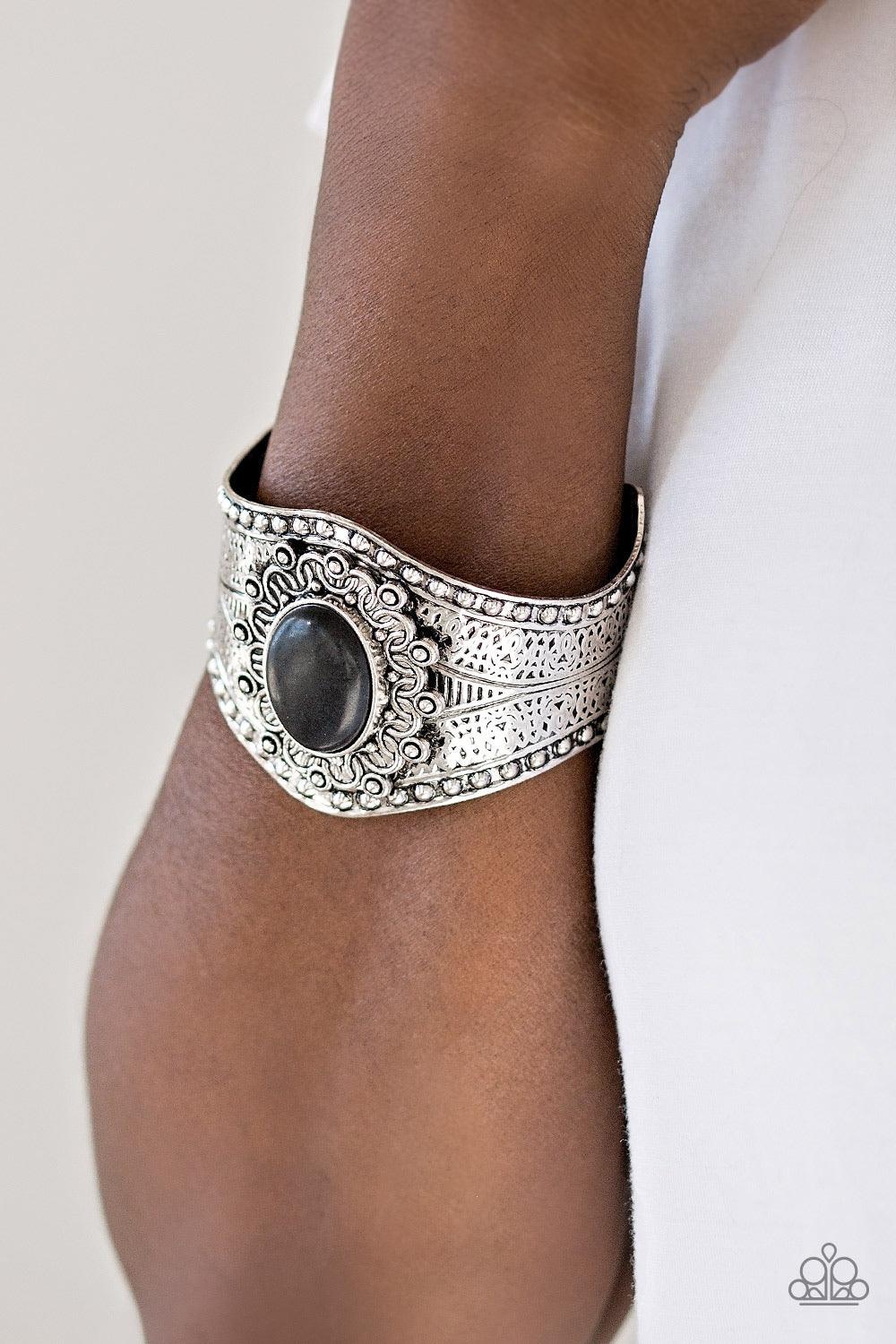 Paparazzi Accessories Mojave Majesty - Black Delicately hammered and studded in tribal inspired textures, a thick silver cuff wraps around the wrist in an artisan inspired fashion. A smooth black stone is pressed into the middle of a silver sunburst patte