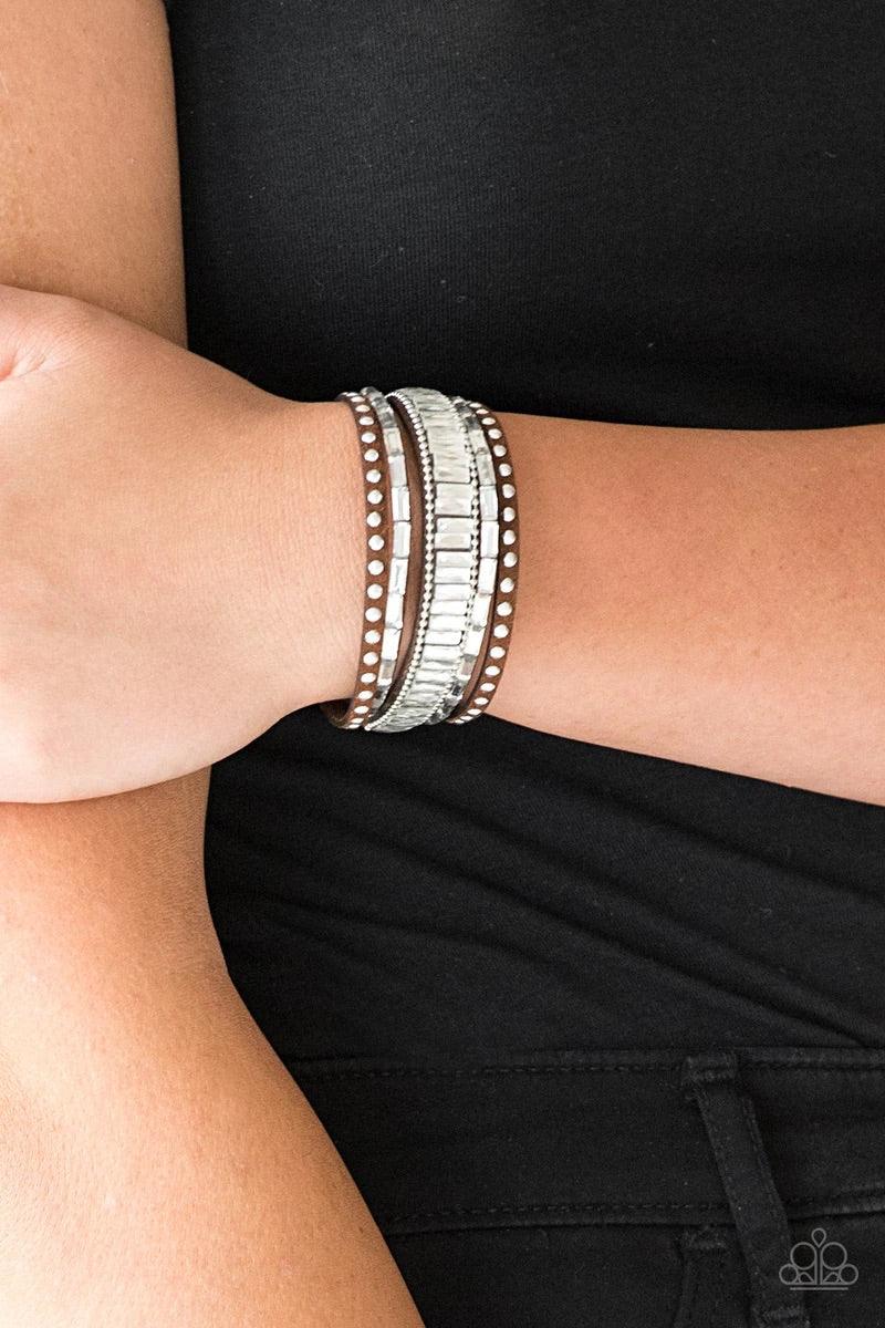 Paparazzi Accessories Rock Star Rocker - Brown Shiny silver studs, dainty silver ball chains, and edgy white emerald-cut rhinestones race along a spliced brown suede band for a rock star look. Features an adjustable snap closure. Sold as one individual br