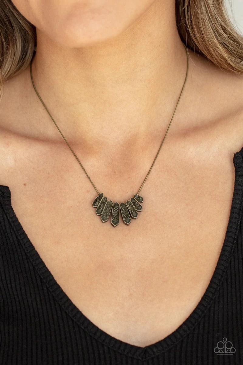 Paparazzi Accessories Monumental March - Brass A row of brass obelisk-like monuments gradually decrease in size as they fan out across the collar. Delicately embossed with textured diamond shapes, they march along a dainty round brass chain. Features an a