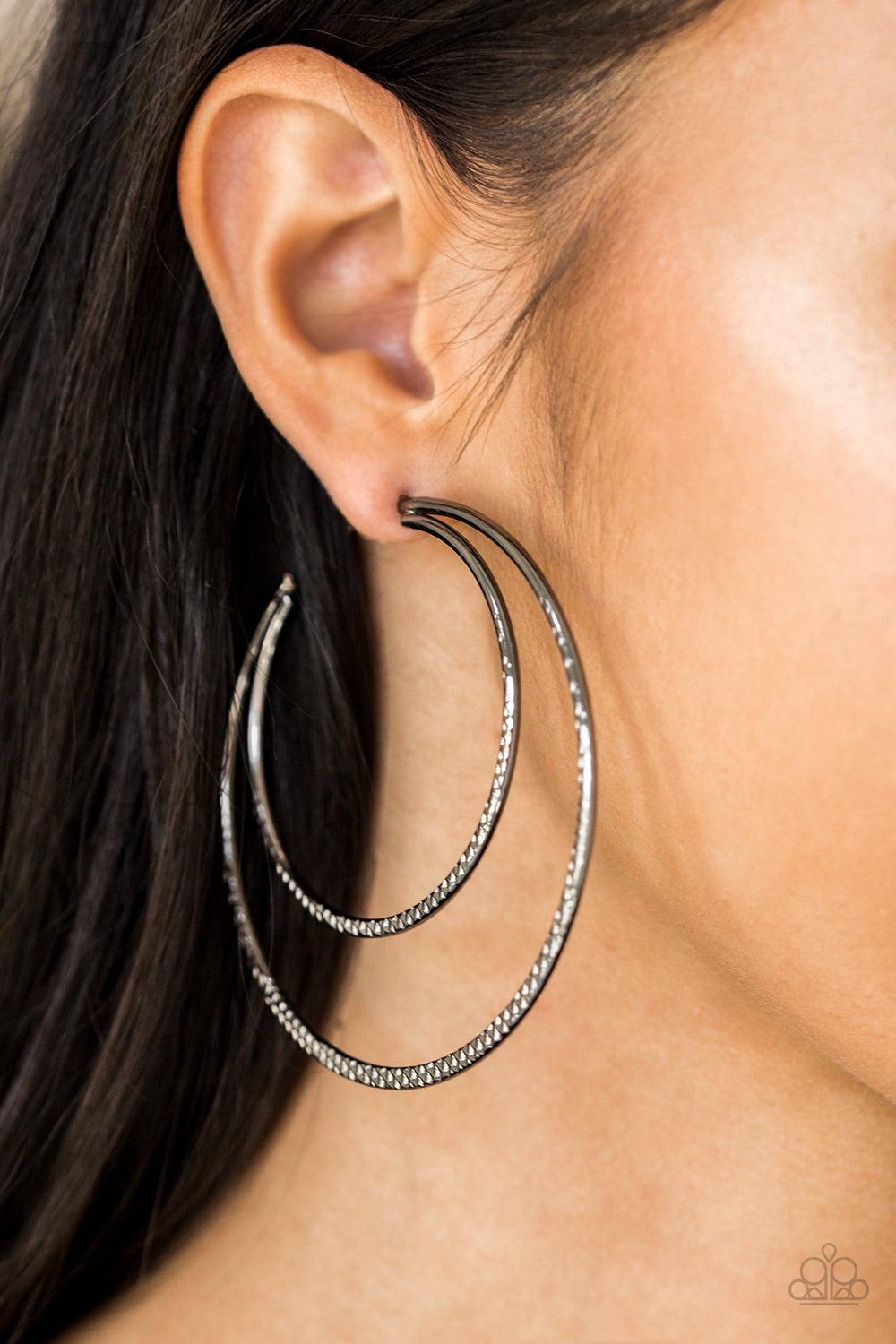 Paparazzi Accessories Drop It Like It’s HAUTE - Black Featuring diamond-cut textures, two glistening gunmetal bars curl into a bold hoop for a flawless finish. Earring attaches to a standard post fitting. Hoop measures 2 3/4” in diameter. Jewelry