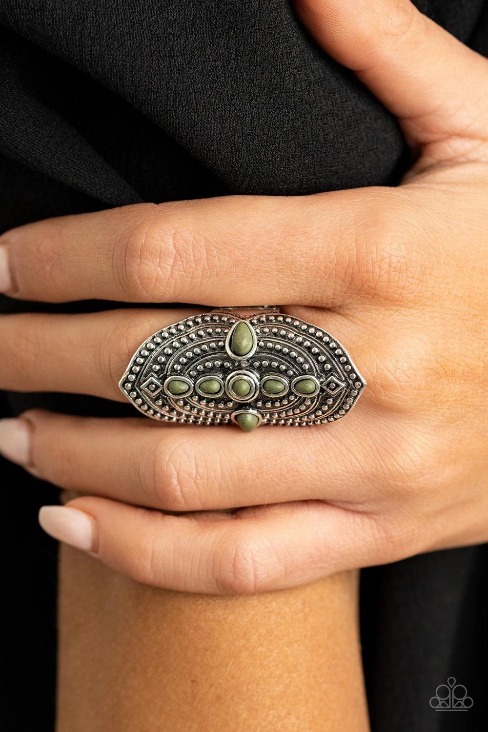 Paparazzi Accessories Shield In Place - Green A dainty collection of imperfect green stones adorn the center of an oversized frame radiating with antiqued studs for a bold tribal inspired look. Features a stretchy band for a flexible fit. Jewelry