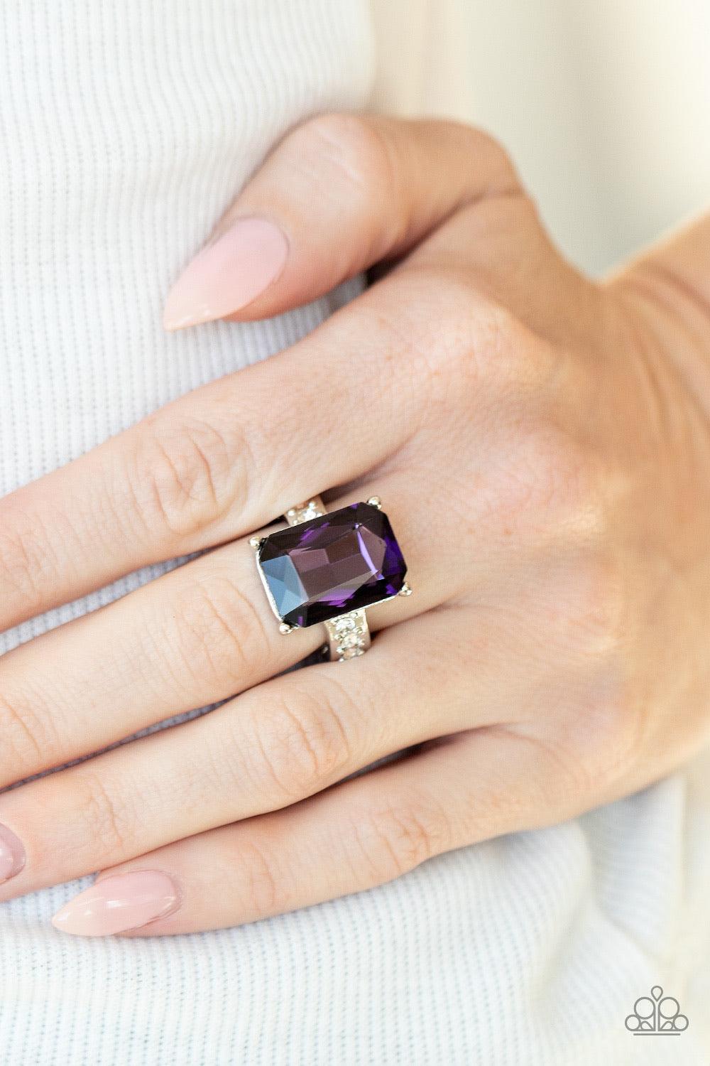 Paparazzi Accessories Bring Down the POWERHOUSE - Purple Featuring an elegant emerald-style cut, an oversized purple gem is pressed into the center of a dainty silver band dotted in glassy white rhinestones for a show-stopping sparkle. Features a dainty s