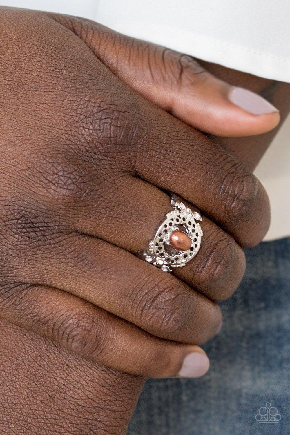 Paparazzi Accessories Mod Modest - Brown Dotted with glittery white rhinestones, an airy filigreed silver band arcs across the finger in a regal fashion. A pearly brown bead is pressed into the center of the band for a timeless finish. Features a stretchy
