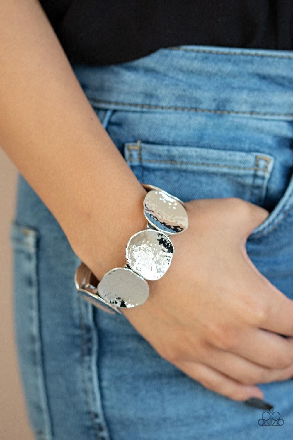 Paparazzi Accessories Treasure Cache - Silver Delicately hammered in shimmer, asymmetrical silver discs are threaded along a stretchy band around the wrist for an edgy look. Jewelry