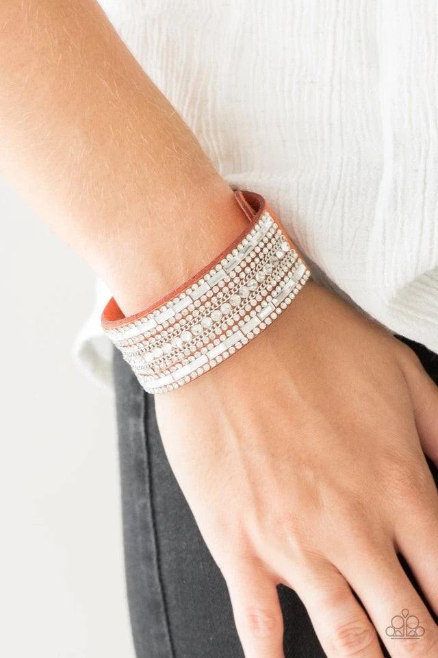 Paparazzi Accessories Rebel Radiance - Orange Featuring classic round and edgy emerald style cuts, glittery white rhinestones and glistening silver chains are encrusted along bands of orange suede for a sassy look. Features an adjustable snap closure. Jew