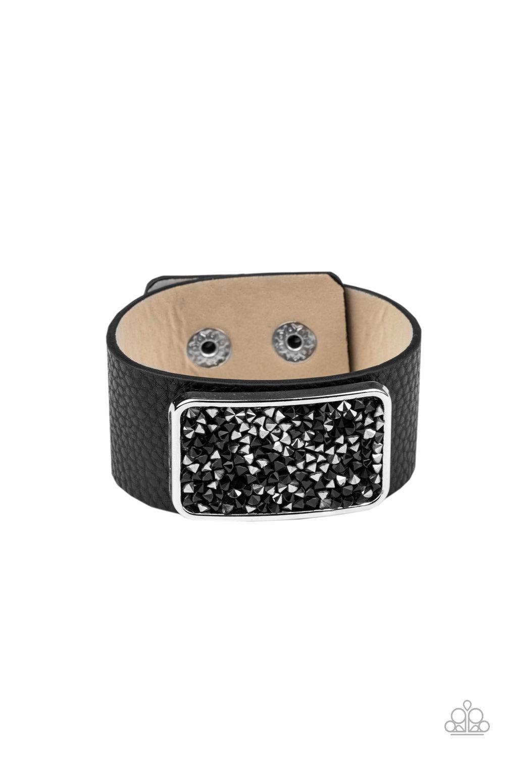 Paparazzi Accessories Interstellar Shimmer - Black A collision of black and hematite rhinestones collect inside a silver rectangular frame that is studded in place in the center of a thick black leather band, creating a sparkling statement piece around th
