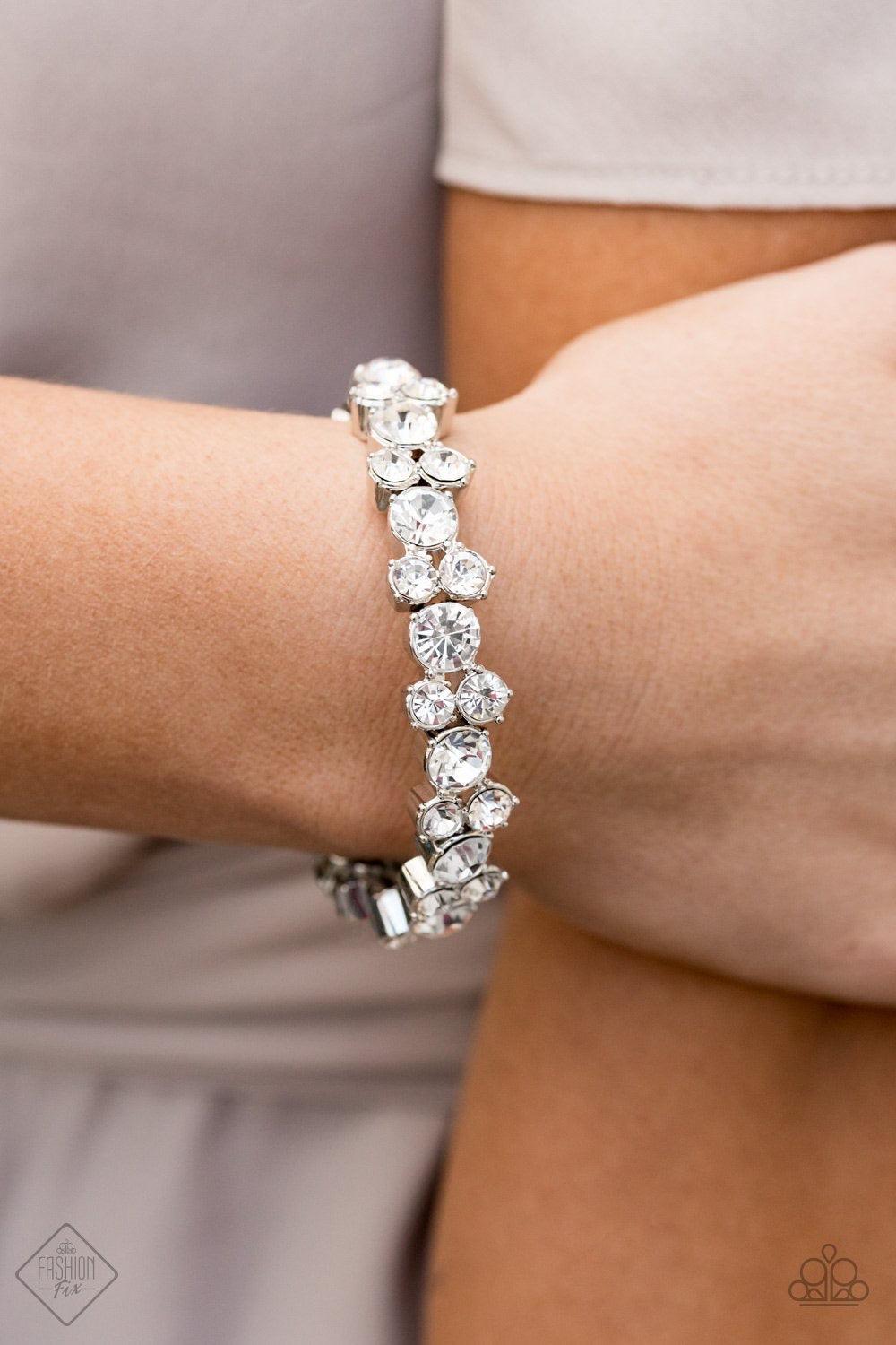 Paparazzi Accessories Here Comes The Bribe - White Featuring sleek silver frames, trios of glittery white rhinestones are threaded along stretchy bands around the wrist for a timeless shimmer. Jewelry