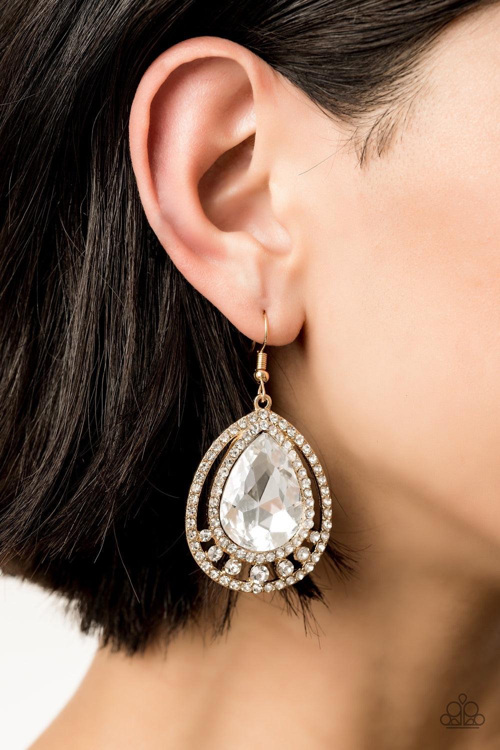 Paparazzi Accessories All Rise For Her Majesty - Gold A dramatically oversized white teardrop gem is nestled inside doubled gold frames radiating with glassy white rhinestones for a jaw-dropping style. Earring attaches to a standard fishhook fitting. Jewe